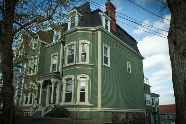 A three-story green siding house is framed by trees.