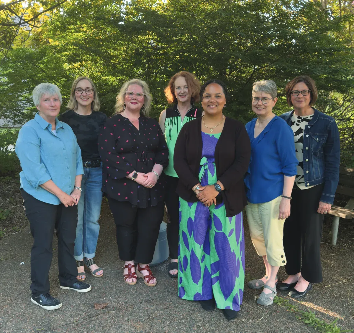 Seven people stand outside posing for a photo in front of a glade of trees.