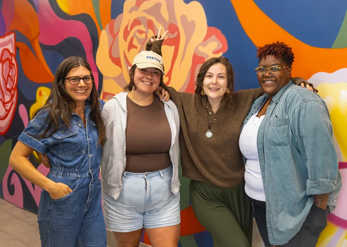 Four people stand posing for a photo in front of a colourful mural painted on a wall.