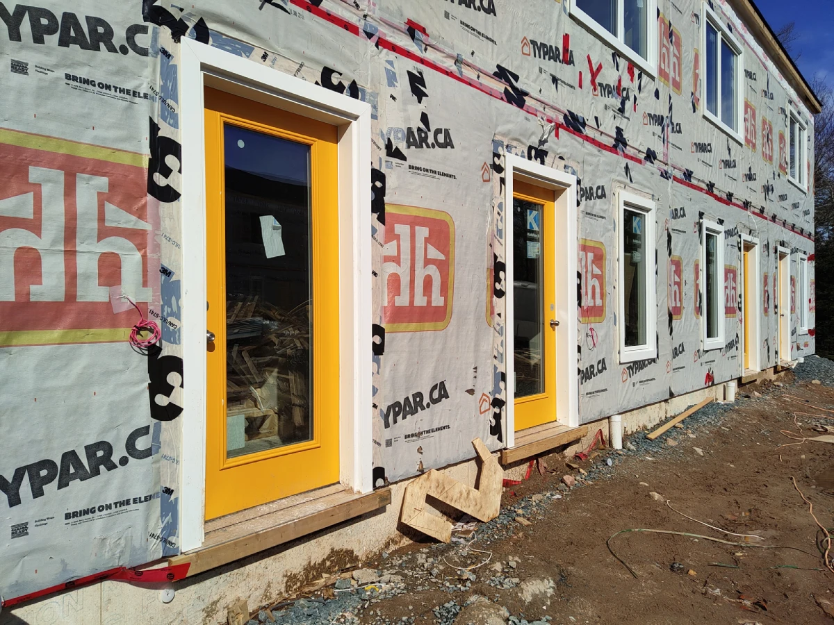 Image of a two-story building under construction. Four yellow doors can be seen surrounded by construction wrapping.