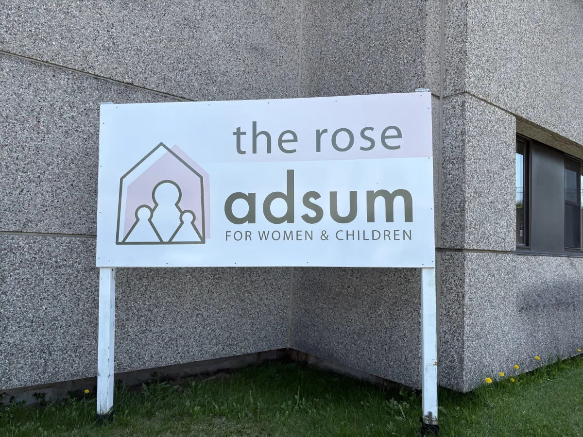 A grey brick building with a large white sign the reads "the rose" with Adsum's logo underneath.
