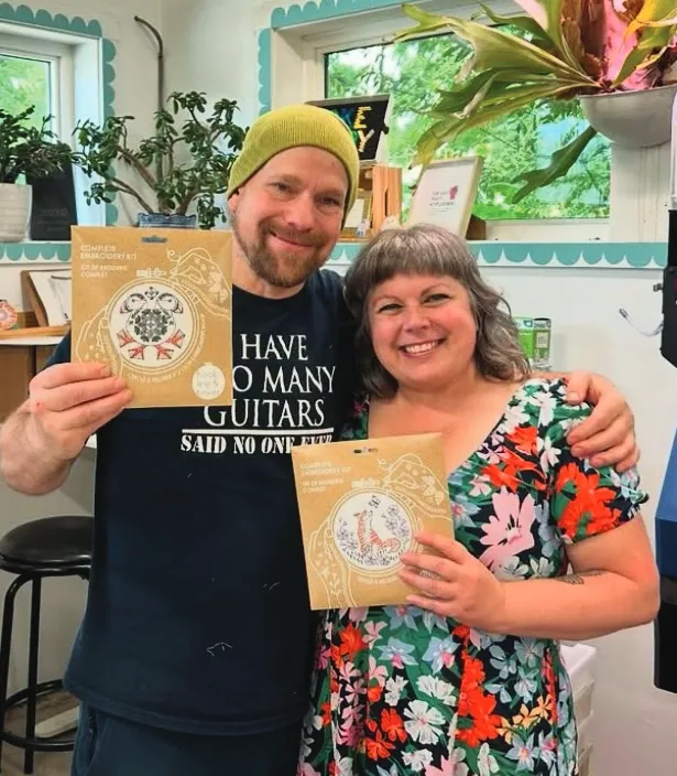 Two people pose for a photo holding embroidery kits.