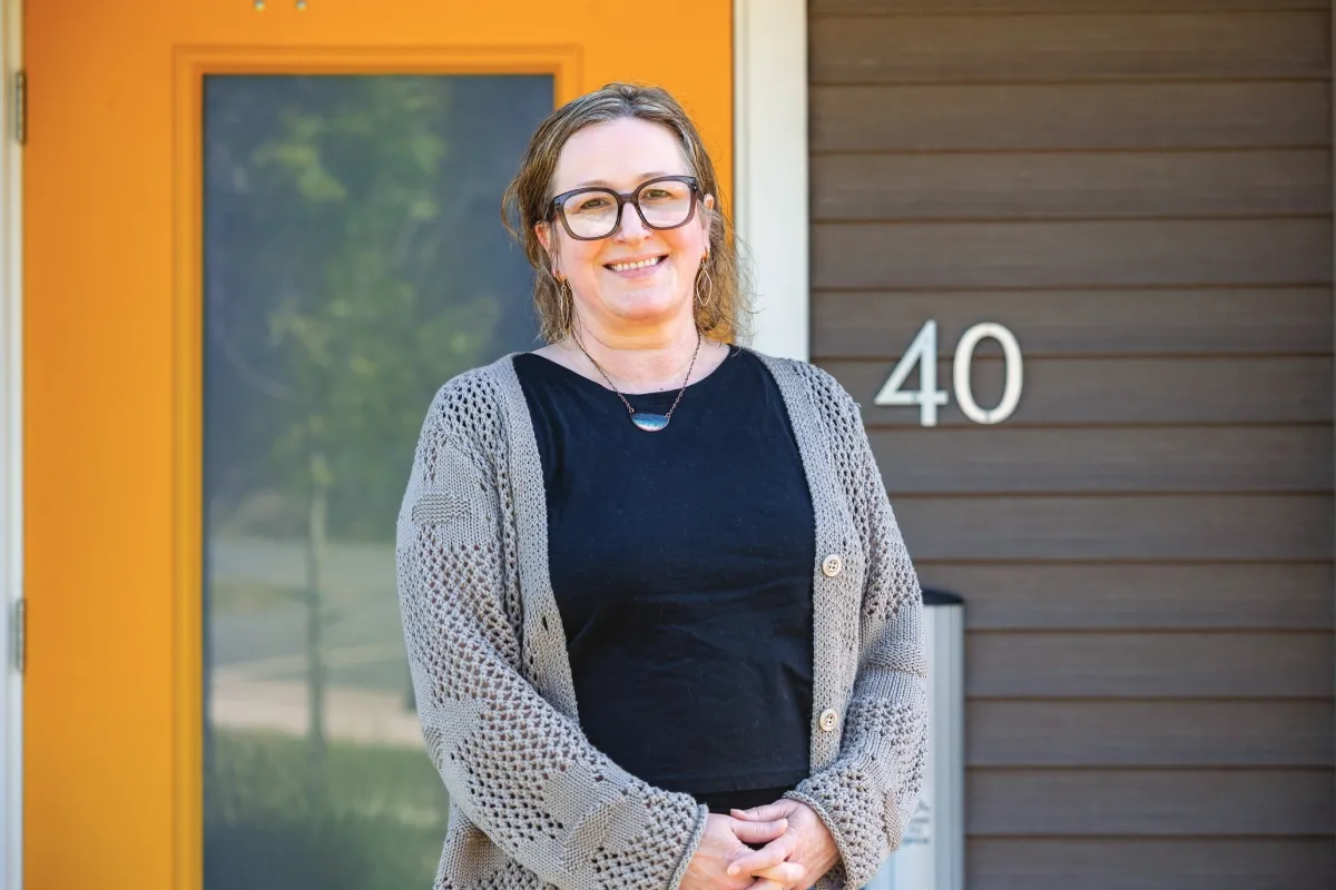 A woman stands smiling at the camera in front of a yellow door and an address sign reading "40".